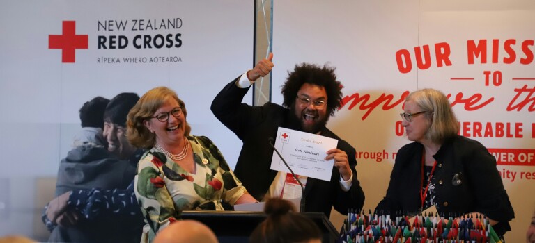 A smiling man holding a certificate, two women on either side of him are smiling and laughing