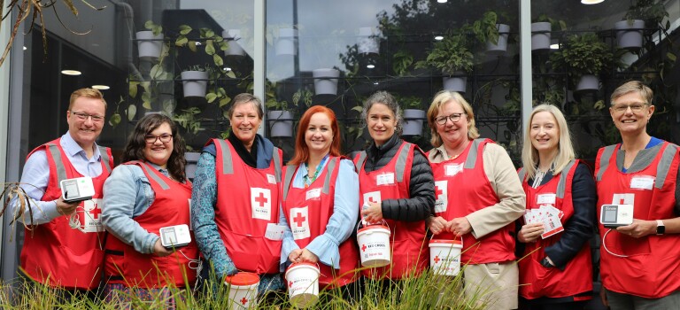 A group of people standing in a line looking at the camera. They're all wearing fundraising bibs and carrying donation buckets. 