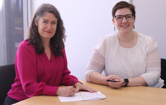 Two women sitting together signing a document