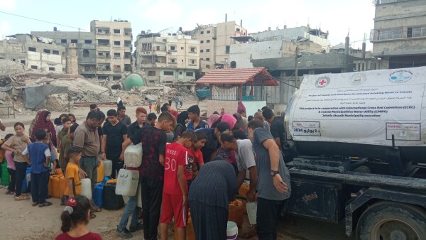 People lining up for water next to a water tanker